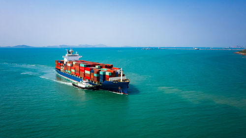 Container ship sailing in green sea and tugboat drag and blue sky background from drone shot