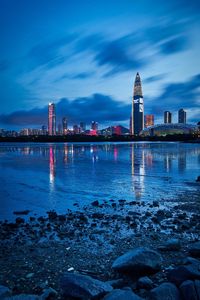 Illuminated city by sea against sky