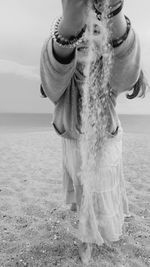 Woman throwing sand while standing at beach against sky