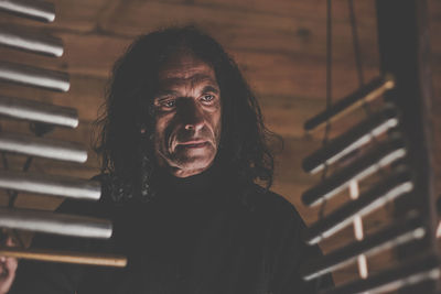 Thoughtful mature man looking away while standing against wooden wall