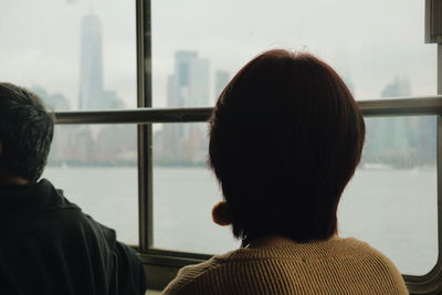 Rear view of woman looking through window while traveling in ferry