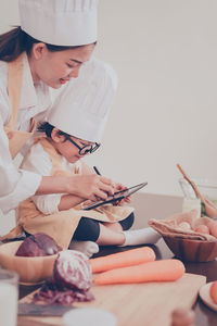 Mother and son wearing chef hats using digital tablet in kitchen