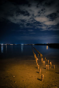 Wooden posts on beach against sky at night