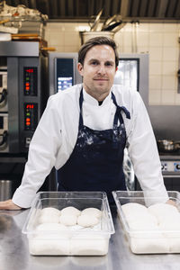 Portrait of confident male chef standing with dough at kitchen counter in restaurant