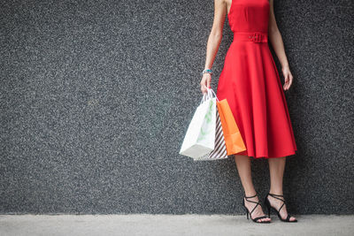 Low section of woman holding shopping bags while standing against wall