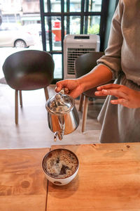 Midsection of barista pouring coffee in cup at cafe