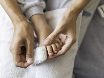 Mother bandages her child big toe. kid foot with bandaged finger. first aid, small domestic injury.