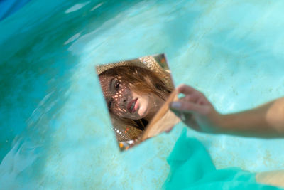 Young woman holding mirror with reflection in wading pool