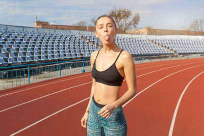 Full length portrait of woman sticking out tongue while standing on running track