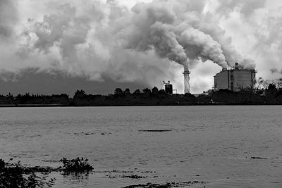 Smoke emitting from factory against cloudy sky