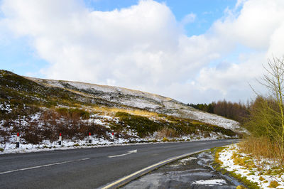 Country road by mountain against sky