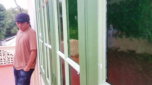 Thoughtful mid adult man standing by window in balcony