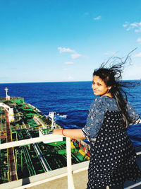 Portrait of smiling woman standing by railing on deck in ship on sea against sky