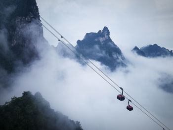 Low angle view of cables hanging on mountain against sky