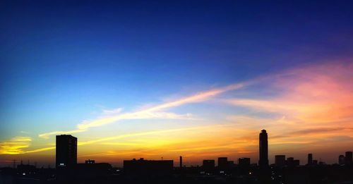 Silhouette of city against cloudy sky during sunset