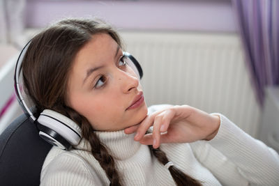 A thoughtful young girl listens to music on wireless headphones.