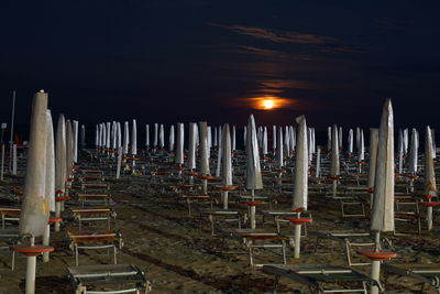 Row of illuminated lights at beach against sky at night