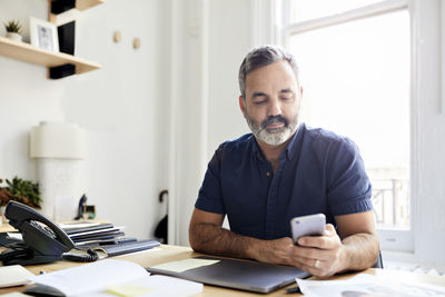 Businessman using smart phone while sitting at desk in creative office