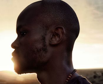 Close-up portrait of shirtless young man against sky