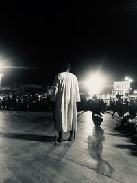 Rear view of man standing on illuminated street at night