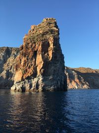 Rock formation by sea against clear blue sky