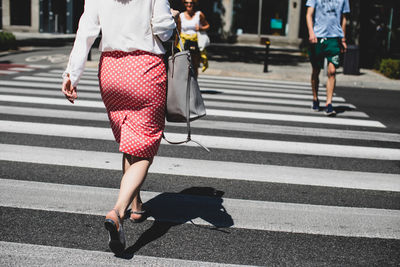 Low section of woman walking zebra crossing during sunny day
