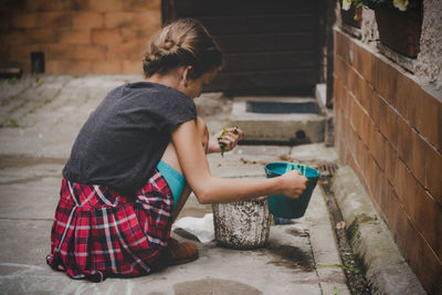 Girl holding bucket while crouching outdoors