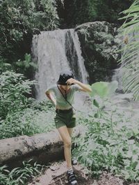 Full length of woman standing on rock against waterfall