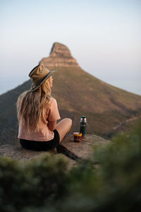 Woman sitting on rock against sky