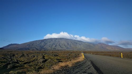 Scenic view of road by mountains against blue sky