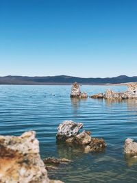 Scenic view of rocks in sea against clear blue sky