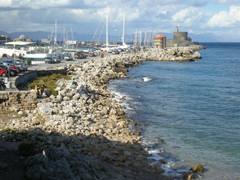 Sailboats on sea by harbor against sky