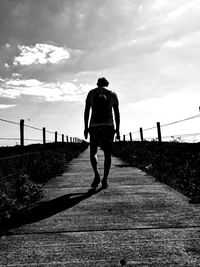 Rear view of man walking on footpath against sky