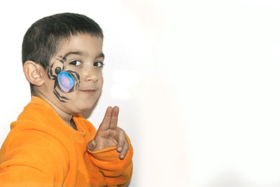 Boy with spider painted on face gesturing peace sign against white background