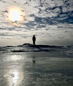 Silhouette man walking on wet beach against sky