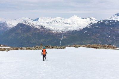 Rear view of man walking on snow covered mountain against sky