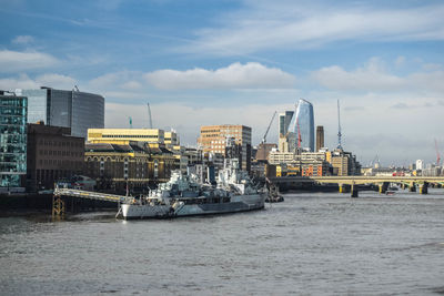 View of hms belfast and london southbank against blue sky with thames in foreground.
