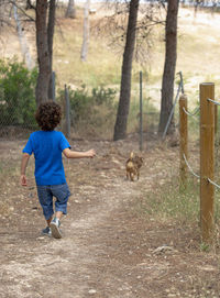 Boy runs downhill playing and chasing his dog on dirt road in a park in the forest