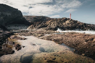 Lighthouse on the thing with waves crashing on rocks with a very calm natural pool