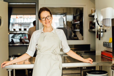 Female chef smiling at camera while standing in restaurant kitchen