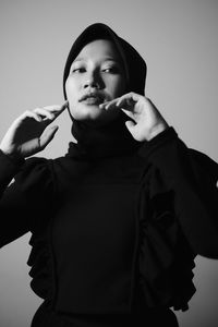 Portrait of woman wearing hood standing against gray background