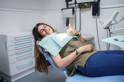 Portrait of smiling young woman showing thumbs up on dentist chair