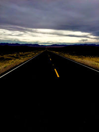Road passing through field against cloudy sky