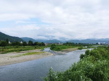 River flowing by plants against cloudy sky