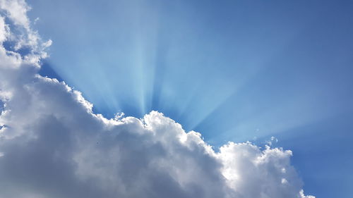 Low angle view of sunlight streaming through clouds