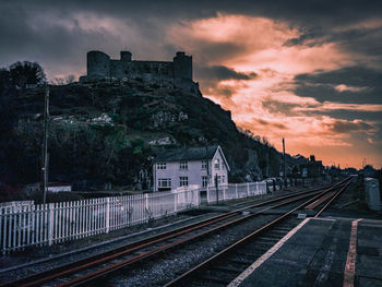 Railroad tracks by buildings against sky during sunset