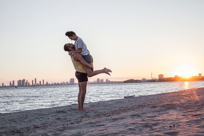 Full length of young man on beach against sky during sunset