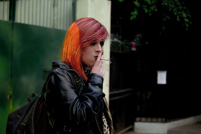 Young woman smoking while standing against wall