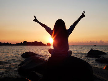 Silhouette woman on rock at beach against sky during sunset