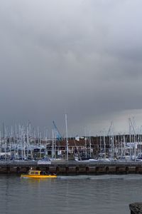 Boats in harbor against cloudy sky